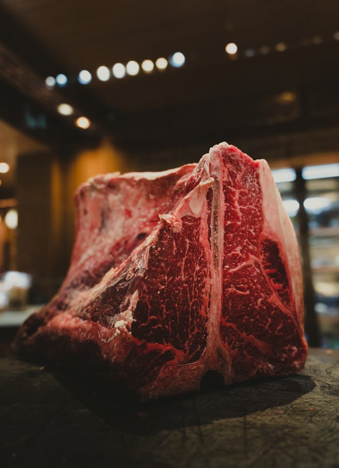 Close-up of a raw marbled beef cut on a wooden surface in a warm kitchen setting.
