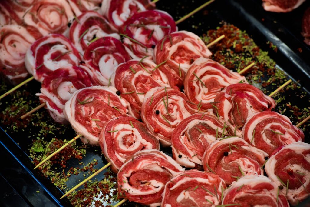 Close-up of raw red meat skewers with spices and herbs, showcasing freshness and marbling.